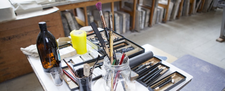 Materialer i æsker, krukke og glas på bord i Laboratoriet for Dybtryk, Højtryk og Litografi